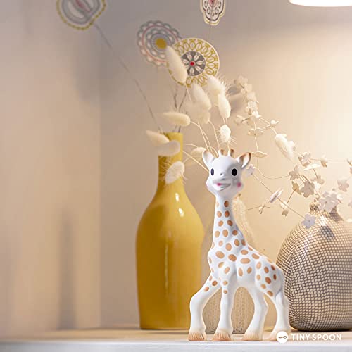Zdjęcie poglądowe żyrafy Sophie la girafe na półce obok wazonu i dekoracji.