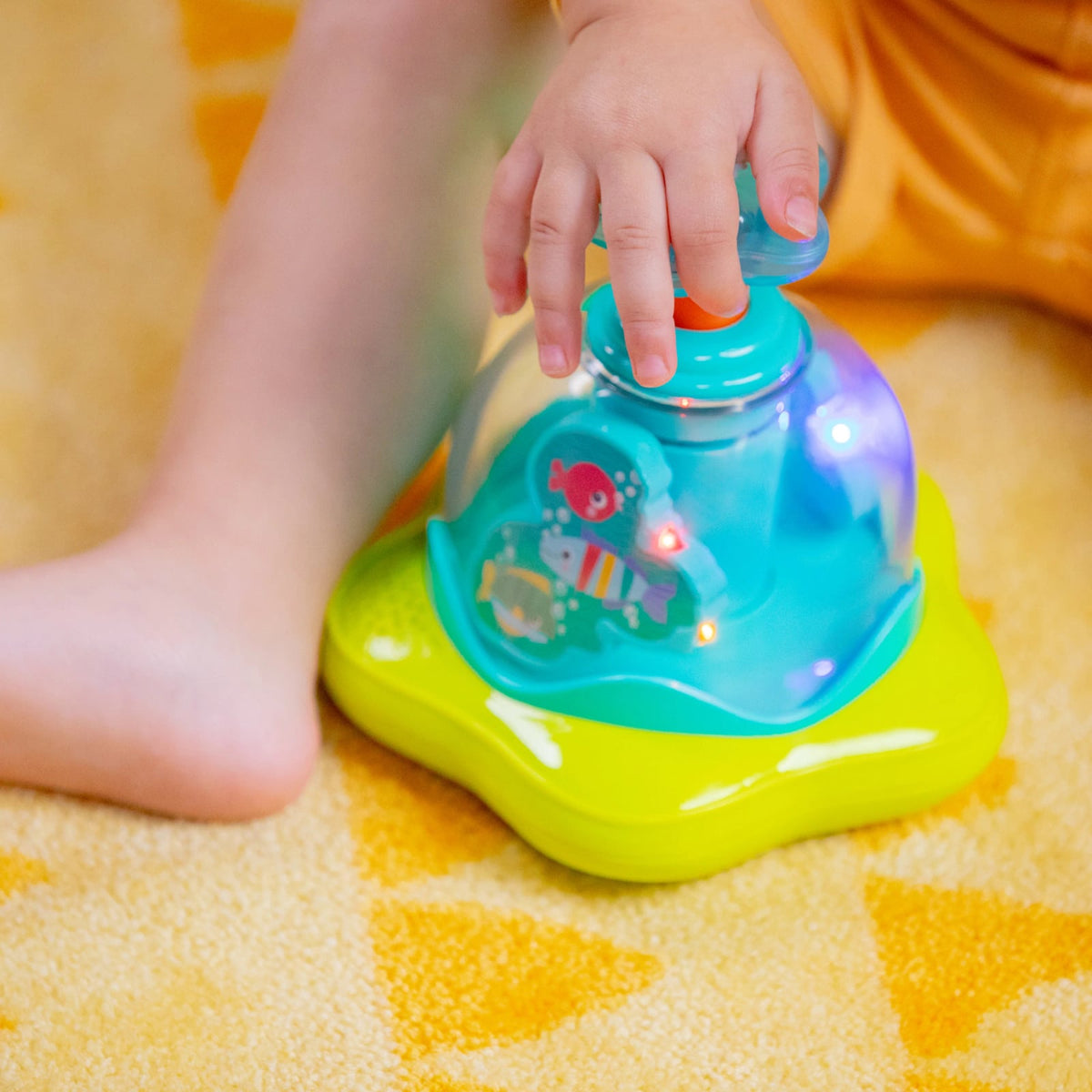 Dłoń dziecka naciskająca przycisk zabawki Bright Starts Press Glow Spinner.