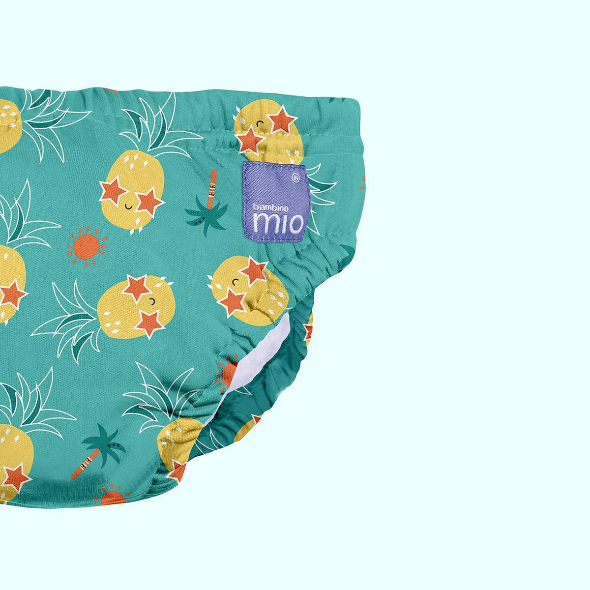 Zbliżenie turkusowej pieluszki Bambino Mio z ananasami i fioletową metką przy brzegu.